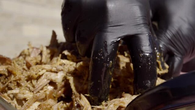 Hands with black gloves, shred the meat of a Pulled Pork just out of the oven.