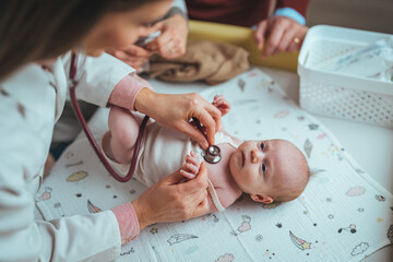 Newborn lying on back while doctor listening to his heartbeat with stethoscope at hospital. Close...