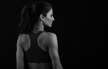 Smiling happy female sporty muscular with ponytail with perfect healthy posture of shoulders, blades and arms in sport bra, standing on dark grey background with empty copy space.