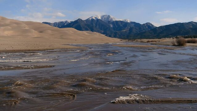 Spring at Medano Creek - Medano Creek rushing down a sandy valley at base of rolling Great Sand Dunes and snow-capped Mt Herard on a sunny Spring morning. Great Sand Dunes National Park, Colorado, USA