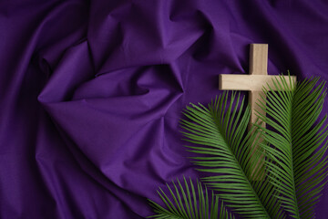 Wood cross and palm leaves on a dark purple fabric background