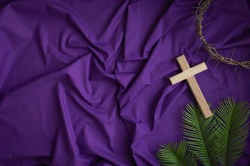 Border of cross, partial crown of thorns and palm leaves on a dark purple fabric background with copy space