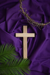 Wood cross, partial crown of thorns and palm leaves on a dark purple fabric background with copy...