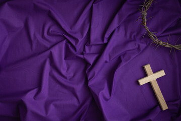 Wood cross and crown of thorns border on a dark purple fabric background with copy space