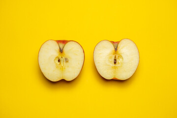 A juicy organic red apple cut in half on a yellow background. Cool minimal flat lay, copy space