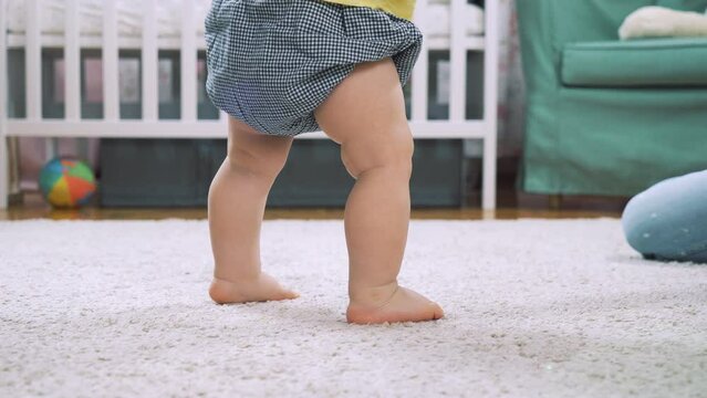 Baby learning to walk taking first steps at home. Little feet walking on floor at living room