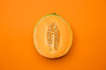 Half melon fresh organically grown on orange background. Sweet and juicy summer fruit. Cool minimal flat lay, copy space