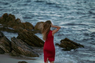 Point of view horizontal shot of a blond woman in a red dress on a Sardinian rocky beach with hands...