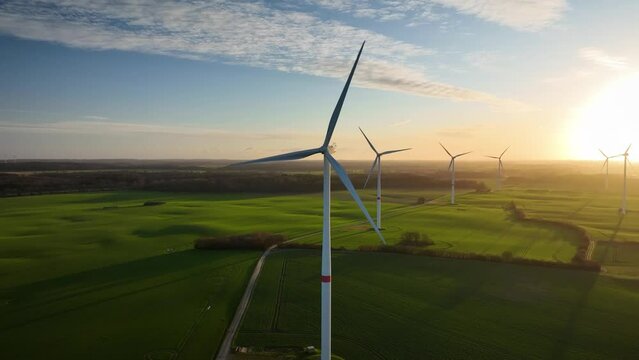 Aerial footage of large spinning wind turbine in agriculture fields Aerial footage of rotating blades of wind turbine against sunset. Aerial flying over renewable energy wind farm.