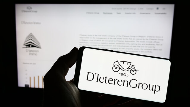 Stuttgart, Germany - 03-18-2023: Person holding smartphone with logo of Belgian automotive company D'Ieteren S.A. on screen in front of website. Focus on phone display.
