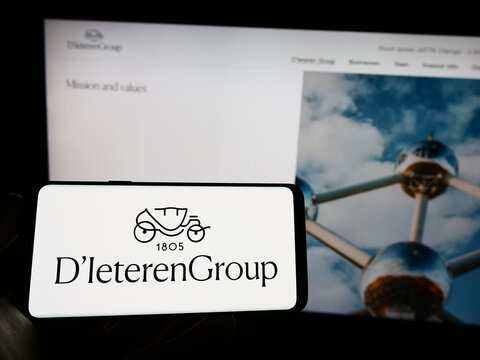 Stuttgart, Germany - 03-18-2023: Person holding mobile phone with logo of Belgian automotive company D'Ieteren SA on screen in front of business web page. Focus on phone display.