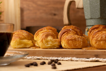Croissants with jelly on wooden board in still life. Coffee beans, cup of coffee and coffee pot. Wood background.