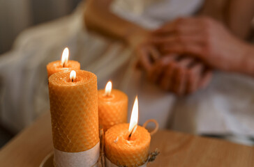 There are burning candles on the table, and the hands of a couple in love are in the background.
