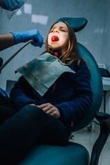 Obraz na płótnie Canvas Dentist, woman doctor in rubber gloves with tools diagnoses, treats teeth from caries of a girl, a child with an open mouth lying in a chair at a dentistry clinic. Close-up photography, medicine.