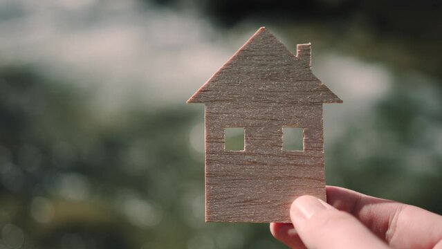 The person is holding in his hand a flat wooden model of the house. Blurred river in slow motion background.