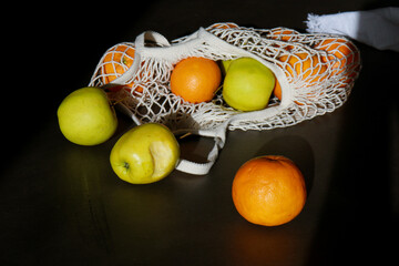  fresh green apples and oranges in cotton string bag on grey table