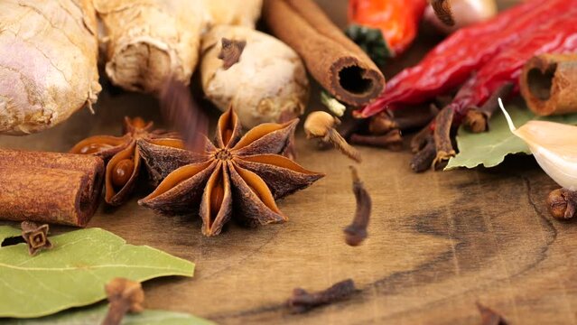 Falling dried clove buds on a wooden board against the background of ginger root, red chili pepper, star anise, bay leaf and garlic.