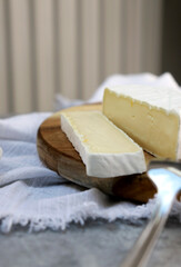 close up of a brie cheese with cut slice on wooden plate