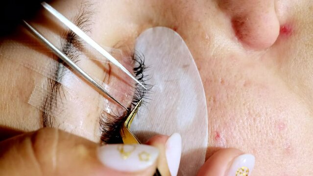 Master sticks artificial eyelashes for client using tweezers. Professional beauty procedure of eyelash extension in salon extreme closeup