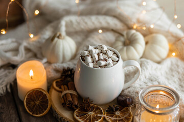 Obraz na płótnie Canvas Autumn cozy home composition with hot chocolate with marshmallow and candles. Aromatherapy on a grey fall morning, atmosphere of cosiness and relax. Wooden background, window sill, close up.