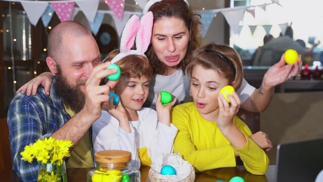 Happy family Easter tradition. Remote greeting relatives using laptop, painting egg, bunny ears. Christian religious holiday Sunday togetherness