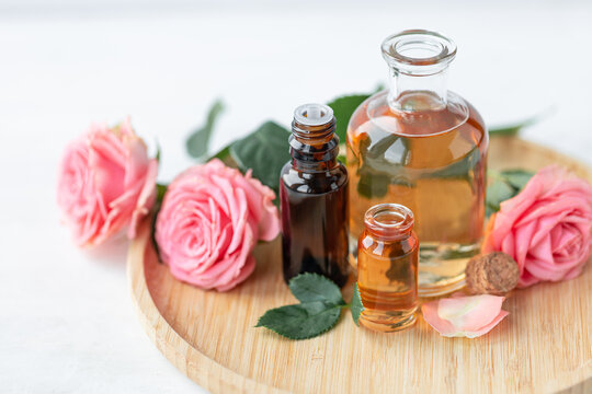 Aromatherapy. Concept of pure organic essential rose oil. Elixir with plant based floral or herbal ingredients. Pink flowers extract. Spa atmosphere with candle, towel. White background