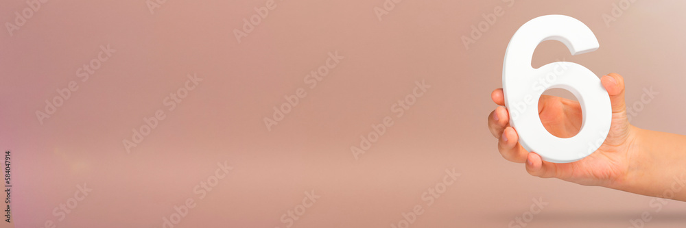 Fototapete number six in hand. a hand holds a white number 6 on a red background with copy space. concept with 