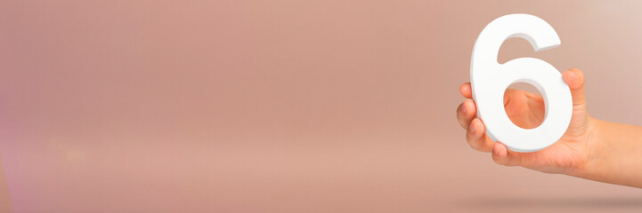 Number six in hand. A hand holds a white number 6 on a red background with copy space. Concept with...