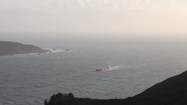 Cargo ship sails by coastal hills with misty horizon in distance