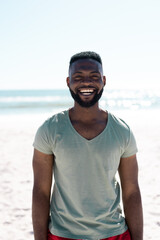 Portrait of cheerful african american bearded man laughing while standing at beach against clear sky