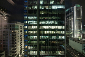 Fototapeta na wymiar Night View of Busy Office Building: Illuminated Windows Reveal Dedicated Employees Working Late