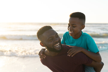 Cheerful african american father piggybacking son against beautiful seascape and clear sky at sunset