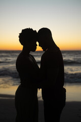 Naklejka premium Silhouette african american romantic couple with head to head standing against sea and clear sky