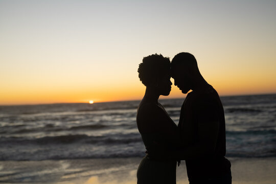 Silhouette african american romantic couple with head to head standing at beach during sunset