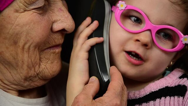 Child with grandmother with phone. The phone is in the hands of a grandmother and a child. Grandmother and granddaughter play with the phone. The girl speaks on the phone. Mobile conversation. 
