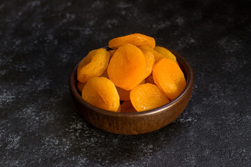 Dried apricot designed on wooden bowl on black surface.Conceptual image