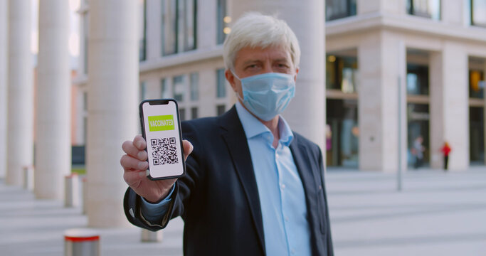 Medium shot of mature businessman in mask showing digital health passport on mobile phone
