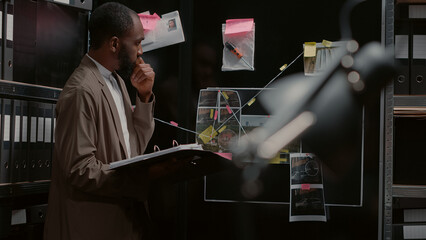 Law enforcement agent looking at detective board, comparing criminal records with new case files. Private officer reading witness statements, holding folder with physical evidence.