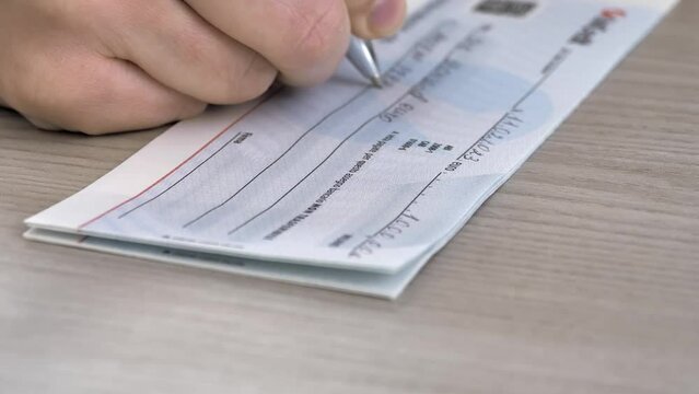 Close-up image of a person's hand filling out a bank check for 1000 euros.