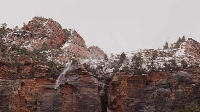 High winds blow the water from this ephemeral waterfall back up and over the face of the red sandstone cliffs that tower above the historic tunnel in Zion Nat. park, Utah, USA on this wet spring day.