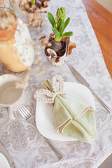 Fototapeta na wymiar Spring festive dining table setting with flowers, napkins and cute bunny decor on linen tablecloth. Easter time. Cozy home