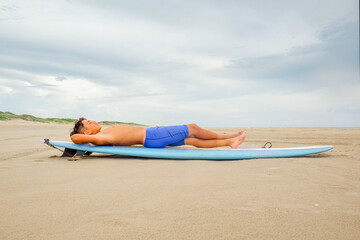 Young preteen boy laying on surfboard on the beach