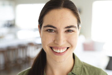 Close-up portrait of smiling caucasian beautiful young woman with brown eyes at home, copy space