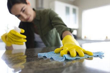 Caucasian young woman wearing yellow washing up gloves cleaning kitchen counter at home