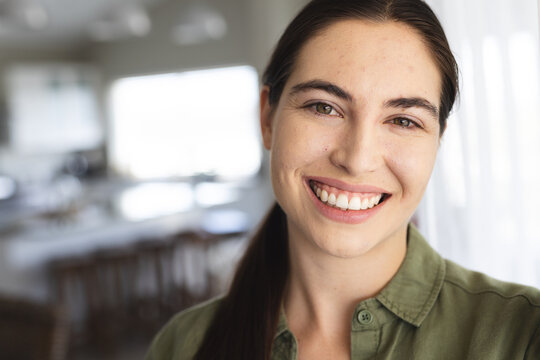 Close-up portrait of smiling beautiful caucasian young woman with brown eyes at home, copy space