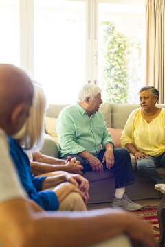 Group of diverse senior friends sitting in living room, talking in group therapy session, copy space