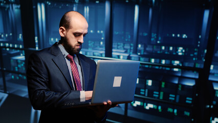 IT server engineer inspecting working computer processor with laptop, standing in professional data center. Infrastructure specialist running hosting server diagnostics. Tripod shot.