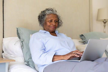 Focused african american senior businesswoman working over laptop while sitting on bed, copy space
