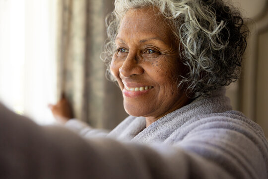 Closeup of smiling african american senior woman opening curtains in the morning after waking up