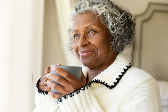 Closeup of thoughtful smiling african american senior woman with coffee cup looking away at home